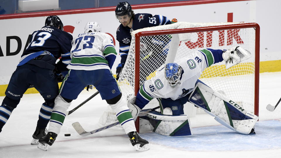 Vancouver Canucks goaltender Thatcher Demko (35) makes a save on Winnipeg Jets' Pierre-Luc Dubois (13) as Canucks' Alexander Edler (23) defends during first period NHL hockey action in Winnipeg, Manitoba on Tuesday March 1, 2021. (Fred Greenslade/The Canadian Press via AP)