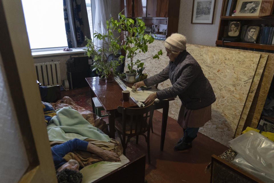 Liudmyla, 78, Mykola's Soloviov wife, lays out sheets of her husband's poems and drawings on the table in the room of their apartment damaged by a missile attack in Sloviansk, a city in Donetsk region, his hometown which lies 25 kilometers from the frontline, Ukraine, Saturday, Jan. 27, 2024. Soloviov, 88, is a painter the world does not know. His expressive and imaginative landscapes of eastern Ukraine encapsulate a lost time, and lie undiscovered, tucked away in a modest home under threat of Russian attack. (AP Photo/Vasilisa Stepanenko)