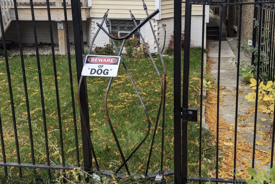 A broken fence with the bars bent, with "Beware of 'dog'" on it