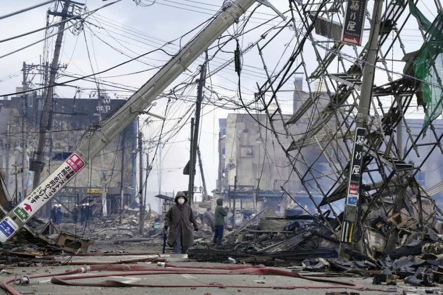 People walk through the damaged marketplace burnt by fire after earthquake in Wajima, Ishikawa prefecture, Japan Tuesday, Jan. 2, 2024. A series of powerful earthquakes hit western Japan, damaging buildings, vehicles and boats, with officials warning people in some areas on Tuesday to stay away from their homes because of a risk of more strong quakes. (Kyodo News via AP)
