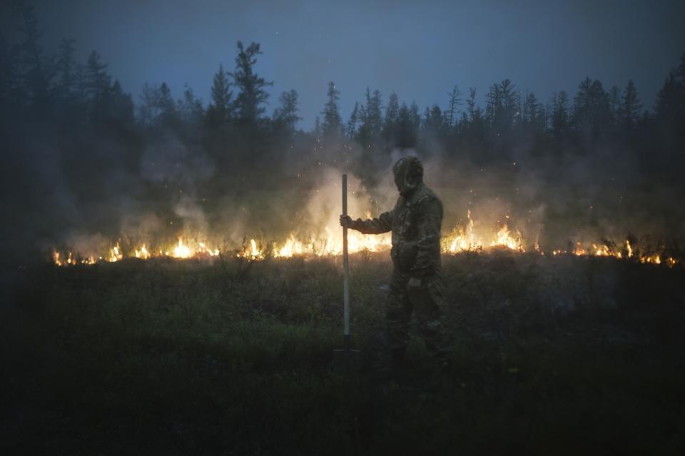 A member of volunteers crew walks past a burning grass near the edge of the fire at Gorny Ulus area west of Yakutsk, Russia, Thursday, July 22, 2021. The hardest hit area is the Sakha Republic, also known as Yakutia, in the far northeast of Russia, about 5,000 kilometers (3,200 miles) from Moscow. About 85% of all of Russia's fires are in the republic, and heavy smoke forced a temporary closure of the airport in the regional capital of Yakutsk, a city of about 280,000 people. (AP Photo/Ivan Nikiforov)