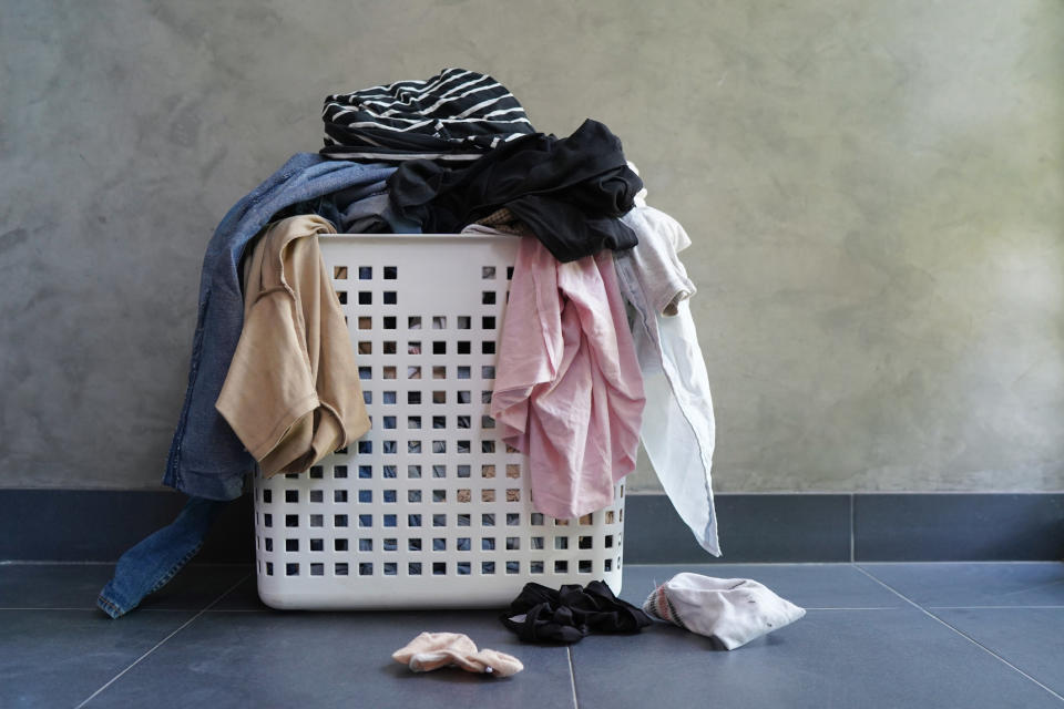 A bunch of clothes messily stuffed in a laundry basket and laying on the floor