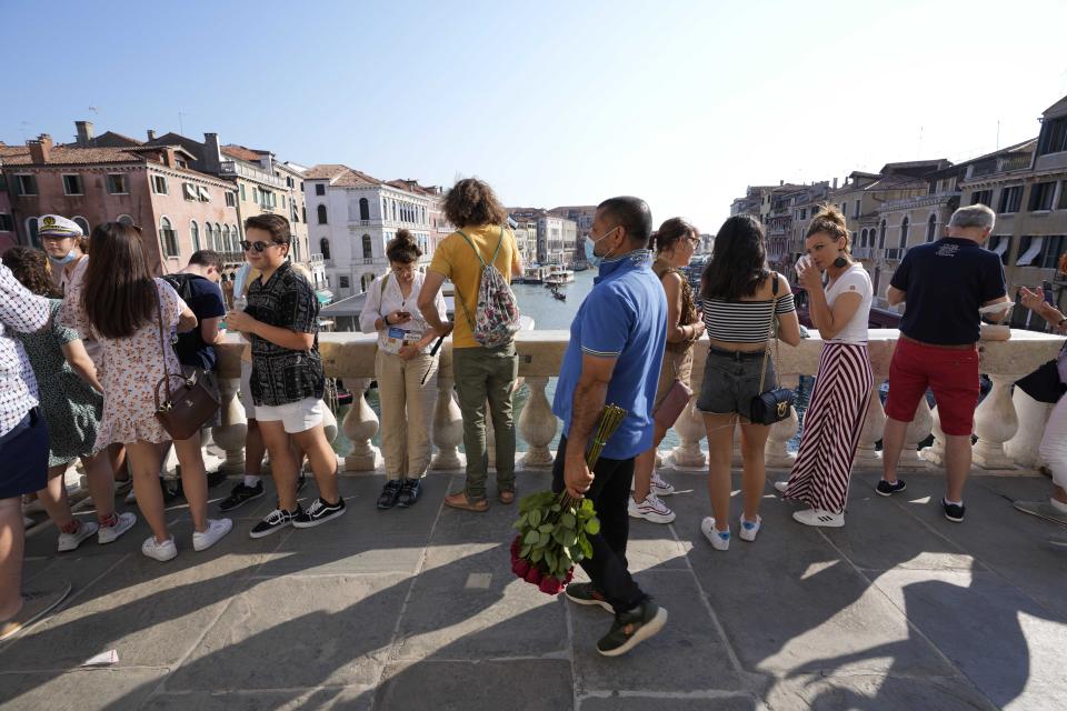 A street vendor sells roses as visitors stand on the Rialto bridge, in Venice, Italy, Thursday, June 17, 2021. After a 15-month pause in mass international travel, Venetians are contemplating how to welcome visitors back to the picture-postcard canals and Byzantine backdrops without suffering the indignities of crowds clogging its narrow alleyways, day-trippers perched on stoops to imbibe a panino and hordes of selfie-takers straining for a spot on the Rialto Bridge or in front of St. Mark’s Basilica. (AP Photo/Luca Bruno)