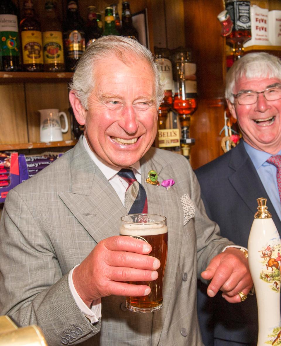 King Charles smiles and holds a pint of beer in Talgarreg, Wales, in 2015.