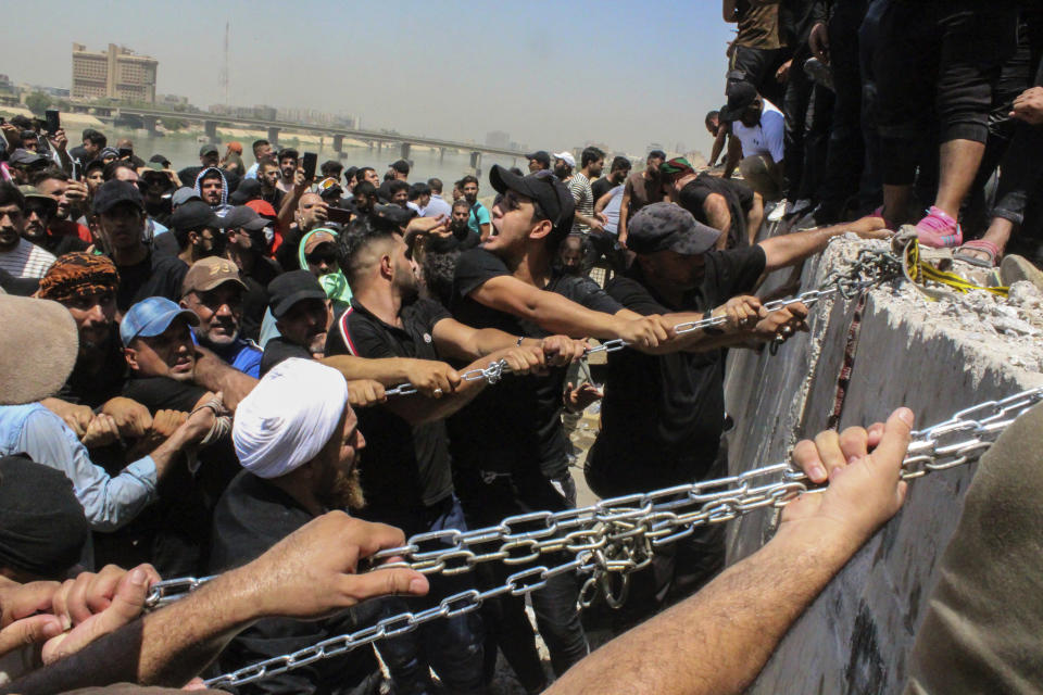 FILE - Protesters try to remove concrete barriers and cross the bridge towards the Green Zone area in Baghdad, Iraq, Saturday, July 30, 2022, as thousands of followers of an influential Shiite cleric breached the building for the second time in a week to protest the government formation efforts lead by Iran-backed groups. Iraq’s two rival Shiite political camps remain locked in a zero-sum competition, and the lone voice potentially able to end the rift — the revered Grand Ayatollah Ali al-Sistani — has been conspicuously silent. (AP Photo/Adil al-Khazali, File)