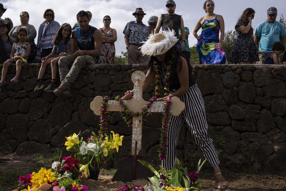 A person places a karone tiare necklace of flowers on the gravesite cross of local horse breeder and former military diver Emilio Araki during his burial at the cemetery in Hanga Roa, Rapa Nui, or Easter Island, Chile, Saturday, Nov. 26, 2022. The first Europeans arrived to Rapa Nui in 1722, soon followed by missionaries, when Rapanui religiosity began to intertwine with Christianity. (AP Photo/Esteban Felix)
