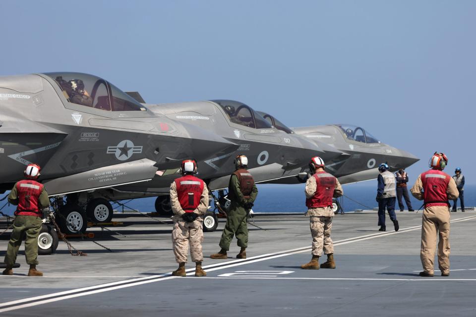 U.K. and U.S. Marine Corps F-35B jets (and their U.K. and U.S. deck crew) prepare to take off from HMS <em>Queen Elizabeth</em> to cross deck to USS <em>Essex</em> on November 8, 2021, while in the Arabian Sea. <em>Crown Copyright</em>