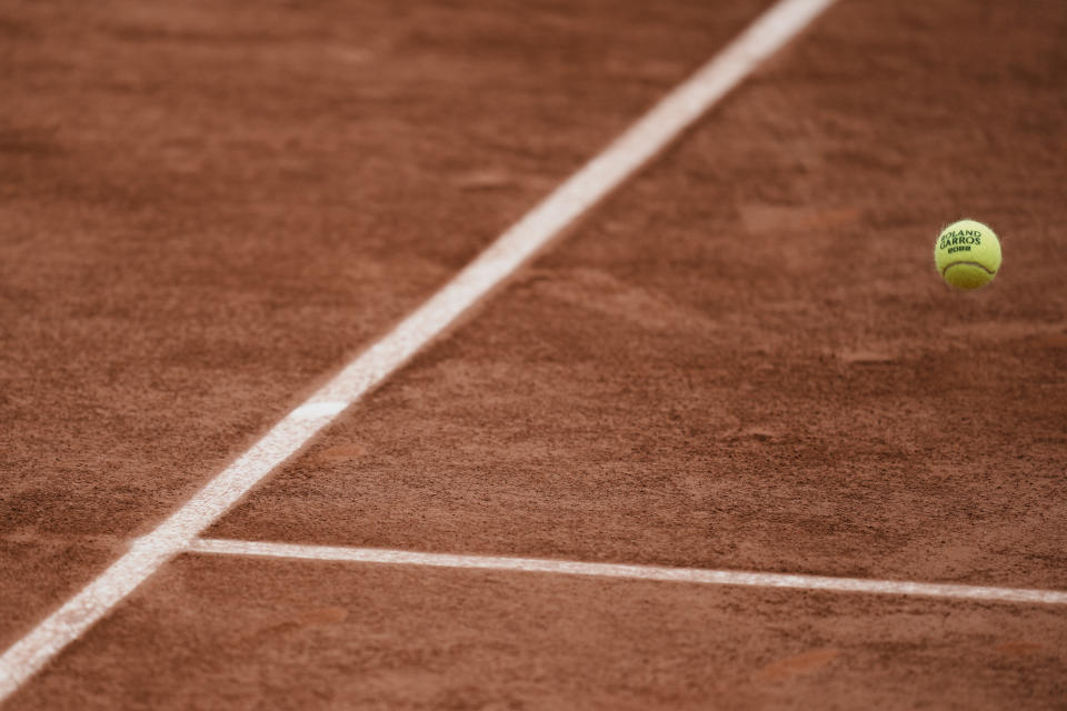 FILE - A Roland Garros 2022 ball flies over the clay court during a second round match at the French Open tennis tournament in Roland Garros stadium in Paris, France, Thursday, May 26, 2022. The French Open is the only Grand Slam tournament held on clay — which actually isn’t truly clay, but the dust from red brick on top of a layer of crushed white limestone. (AP Photo/Thibault Camus, File)