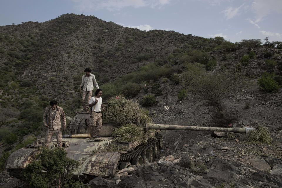 In this Monday, Aug. 5, 2019 photo, fighters from a militia known as the Security Belt, that is funded and armed by the United Arab Emirates, stand on a tank camouflaged with brush, at the Gabhet Hajr frontline with Houthi rebels, in Yemen's Dhale province. Yemen’s civil war has been deadlocked for months, with neither side making major gains. At one of the most active front lines, militiamen backed by the Saudi-led coalition are dug in, exchanging shelling every night with Iranian-allied Houthi rebels only a few hundred meters away. (AP Photo/Nariman El-Mofty)