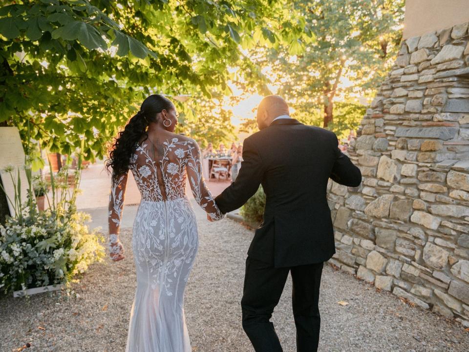 A bride and groom hold hands as they walk away from the camera.