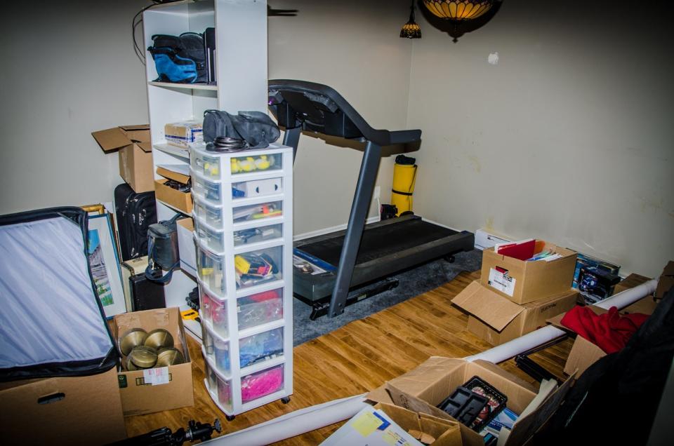 Messy room in basement filled with gym equipment, storage containers, and cardboard boxes.
