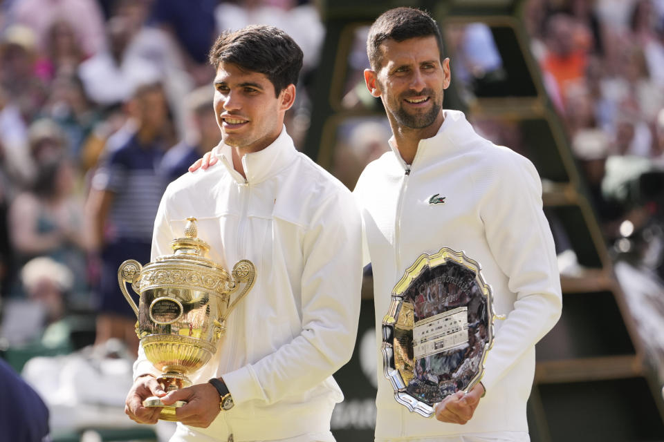 El español Carlos Alcaraz sostiene el trofeo de campeón al lado de Novak Djokovic tras la final de Wimbledon el domingo 14 de julio del 2024. (AP Foto/Alberto Pezzali)