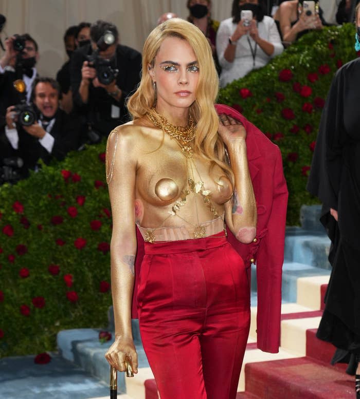 Cara goes topless with a painted body and holds her jacket over her shoulder