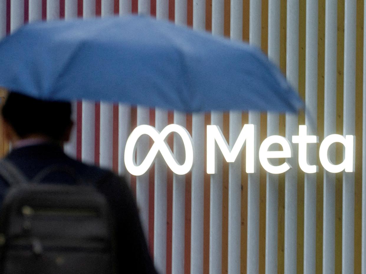 Man with blue umbrella with back against Meta logo.