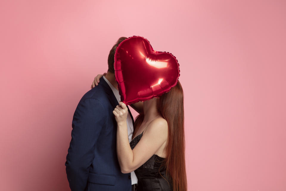 Happy holding balloons shaped hearts. Valentine's day celebration, happy caucasian couple on coral background. Concept of human emotions, facial expression, love, relations, romantic holidays.