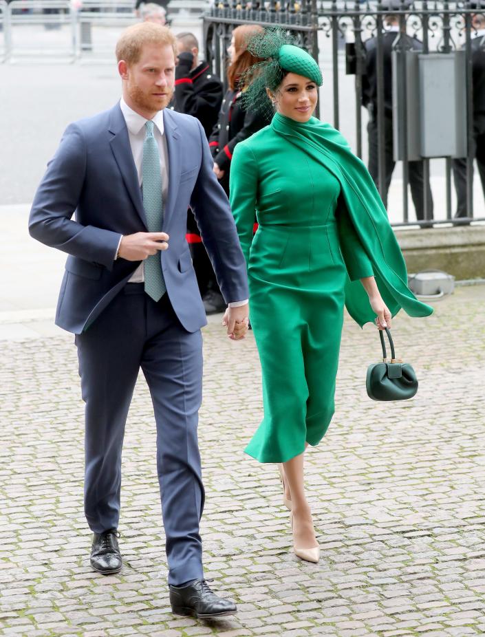 Harry in a grey-blue suit and mint green tie and Meghan in a tea length emerald green cape dress with matching purse and fascinator.