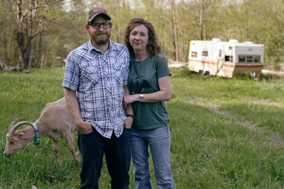 James and Ellie Holden pose with one of their goats and a camping trailer brought when they left California, at their home, Thursday, May 12, 2022, in Proctor, Vt. After fleeing one of the most destructive fires in California, the Holden family wanted to find a place that had not been so severely affected by climate change and chose Vermont. (AP Photo/Charles Krupa)
