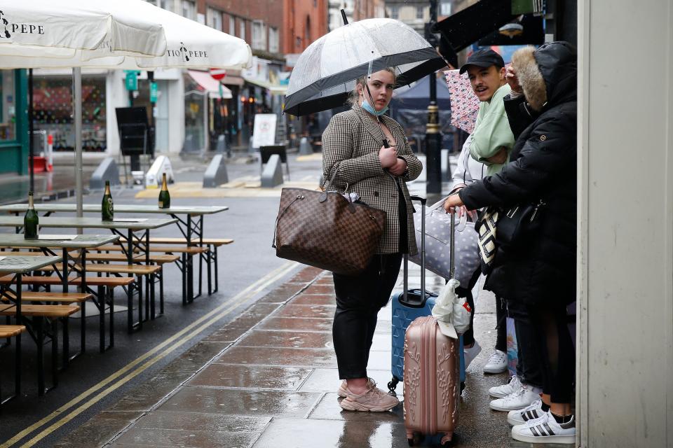 <p>People stand outside in the rain near temporary outdoor seating in Soho</p> (Getty Images)