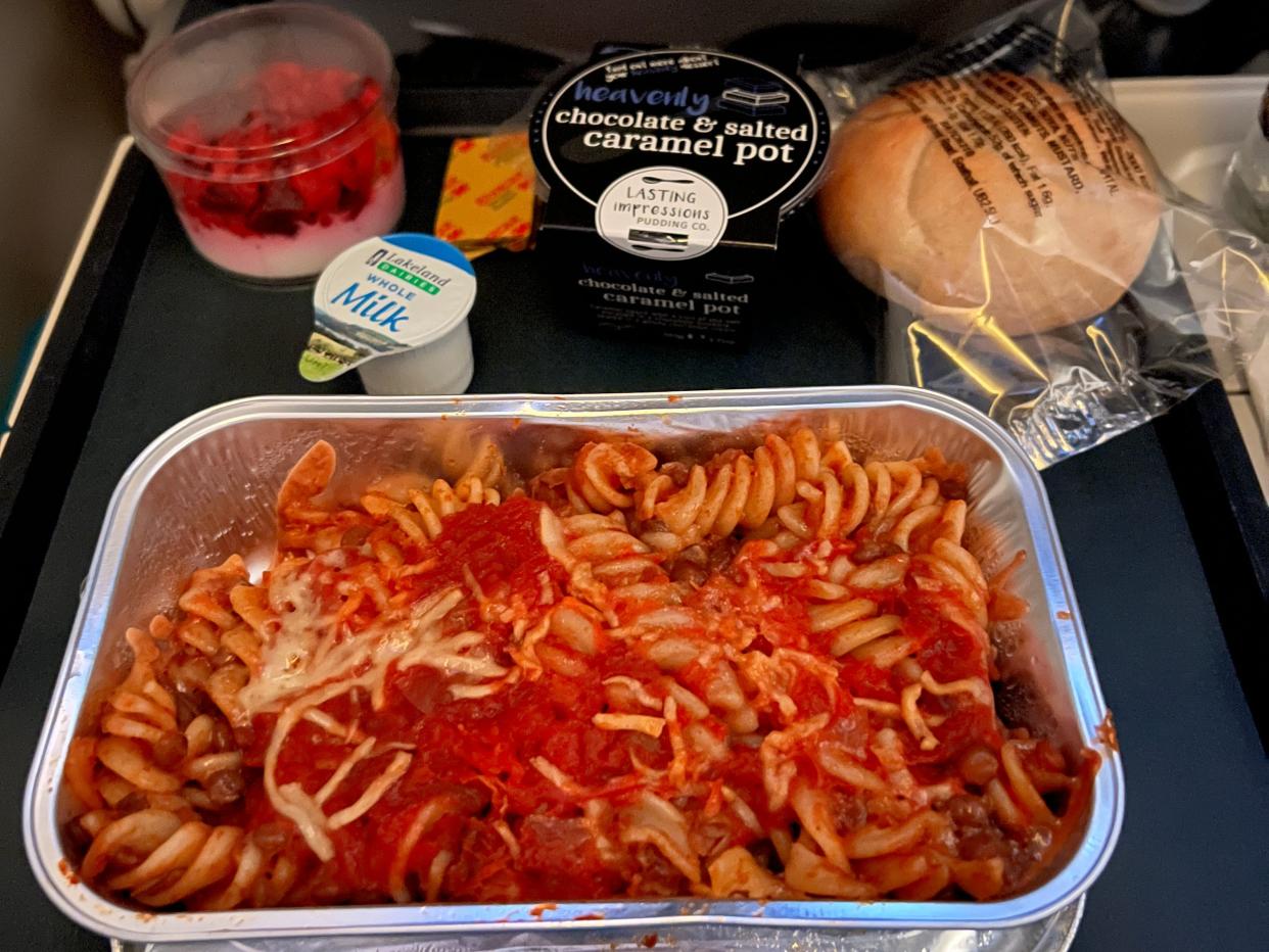 A meal of pasta, a chocolate dessert, fruit pot, and bread roll, flying British Airways economy class