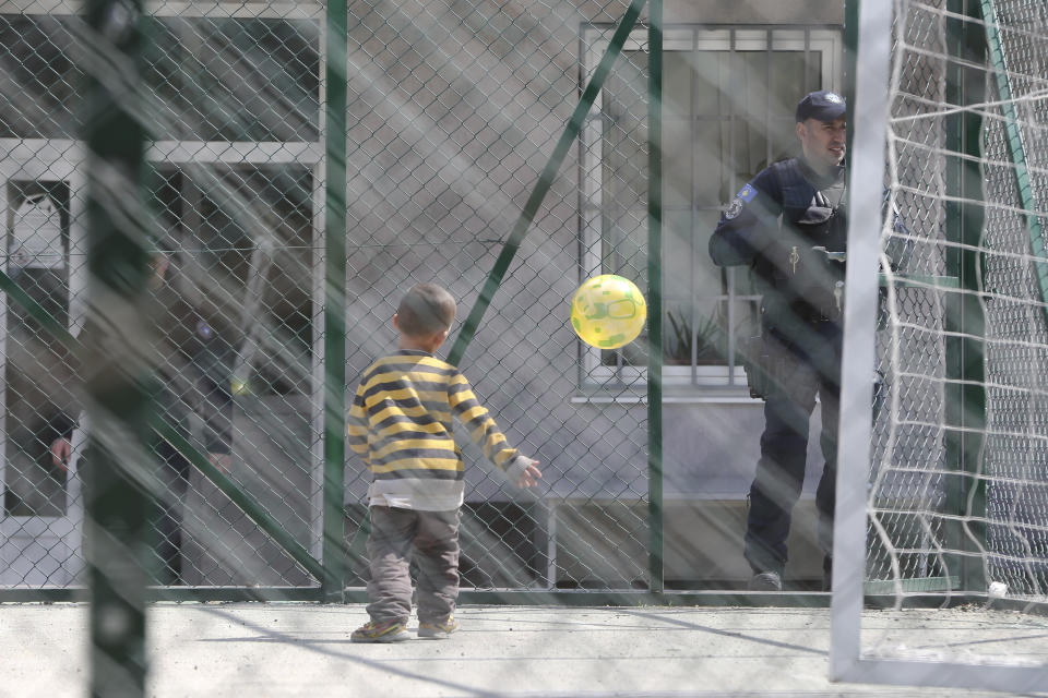 A child plays with a ball near a police officer at a detention center where authorities have brought back from Syria 110 Kosovar citizens, mostly women and children in the village of Vranidol on Sunday, April 20, 2019. Four suspected fighters have been arrested, but other returnees will be cared for, before being sent to homes over the coming days according to Justice Minister Abelard Tahiri. (AP Photo/Visar Kryeziu)