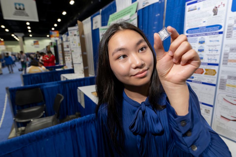 A girl in a blue shirt with long dark hair has a small OETC device that looks like a small clear square with white inside