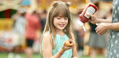 A young girl holding a hot dog next to a man holding a bottle of ketchup