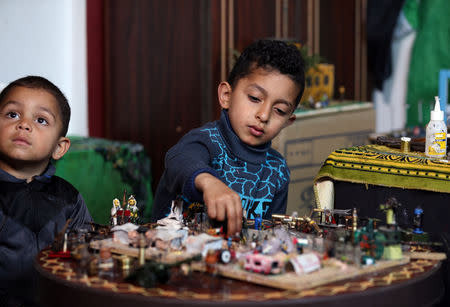 The son of Palestinian diorama artist Majdi Abu Taqeya (C) checks miniature figures that his father carved from remnants of Israeli ammunition collected from the scenes of border protests along the Israel-Gaza border, in the central Gaza Strip March 11, 2019. Picture taken March 11, 2019. REUTERS/Ibraheem Abu Mustafa