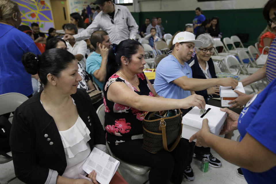 In this Sunday, June 30, 2019 photo Maria Alfaro, center, and her husband Catarino Alfaro, center right, both of Revere, Mass., and immigrants from El Salvador, put money in a collection box at the conclusion of a Temporary Protected Status meeting in Somerville, Mass. TPS is a program that offers temporary legal status to some immigrants in the U.S. who can't return to their country because of war or natural disasters. The donated money was collected to benefit TPS services. (AP Photo/Steven Senne)