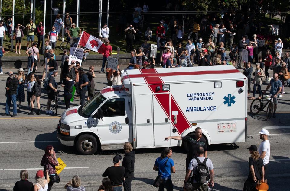 An ambulance passes through a crowd of people protesting COVID-19 vaccine passports and mandatory vaccinations