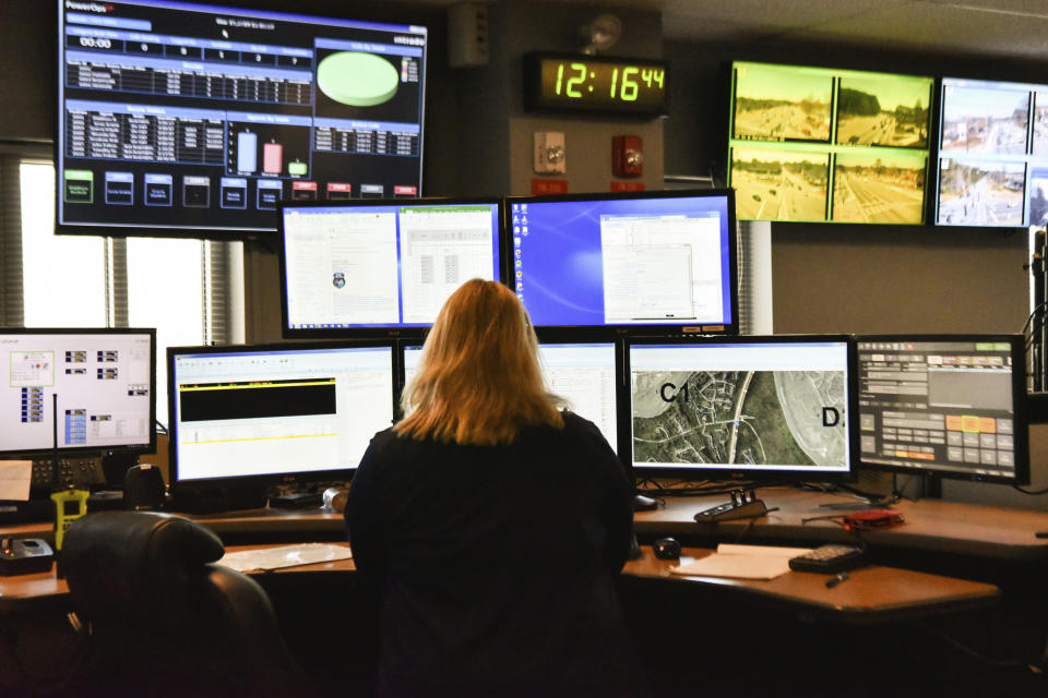 FILE - In this March 15, 2018, file photo, a dispatcher works at a desk station with a variety of screens used by those who take 911 emergency calls. Jobs with state and city governments are usually a source of stability in the U.S. economy, but the financial devastation wrought by the coronavirus pandemic has forced cuts that will reduce public services, from schools to trash pickup. In some areas, 911 calls are taking a longer time to be answered. (AP Photo/Lisa Marie Pane, File)