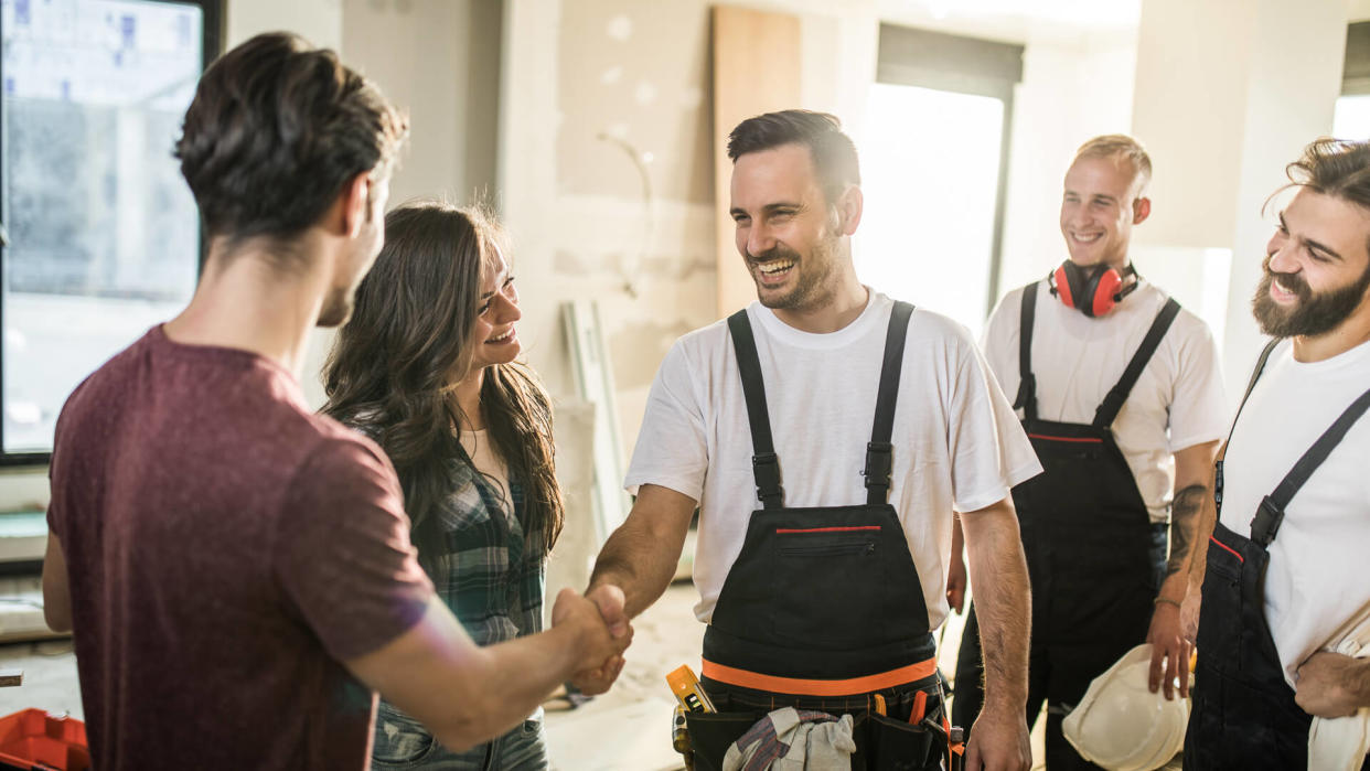 Happy manual worker welcoming young couple to their renovated apartment.