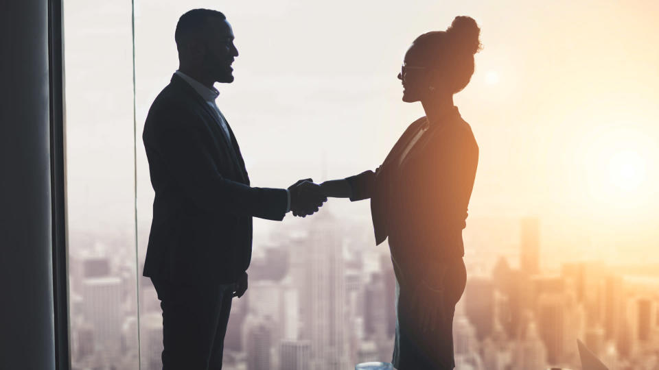 Silhouetted shot of two businesspeople shaking hands in an office.