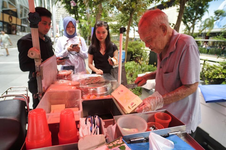 An elderly man slicing a block of durian-flavored ice cream at his cart along Orchard Road, Singapore's main shopping district.