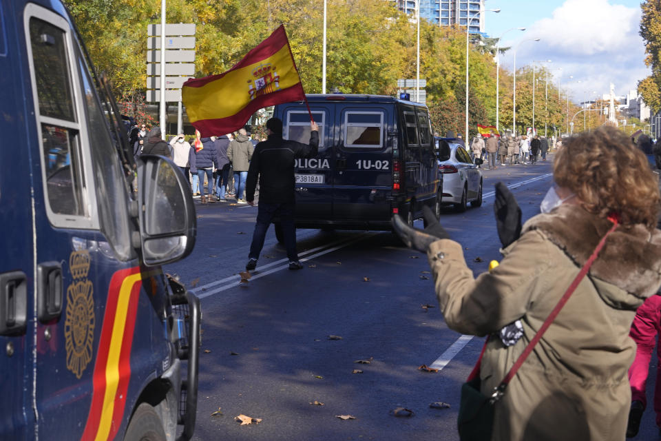 A protester with a Spanish flag walks behind one of the police vans escorting a police protest as people applaud in Madrid, Spain, Saturday, Nov. 27, 2021. Tens of thousands of Spanish police officers and their supporters rallied in Madrid on Saturday to protest against government plans to reform a controversial security law known by critics as the “gag law.” (AP Photo/Paul White)