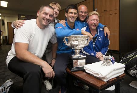 Novak Djokovic (C) of Serbia poses with his coach Boris Becker (R), members of his support team and the men's singles trophy in the player's locker room after he defeated Andy Murray of Britain at the Australian Open tennis tournament February 2, 2015, in this handout courtesy of Tennis Australia. REUTERS/Fiona Hamilton/Tennis Australia/Handout via Reuters
