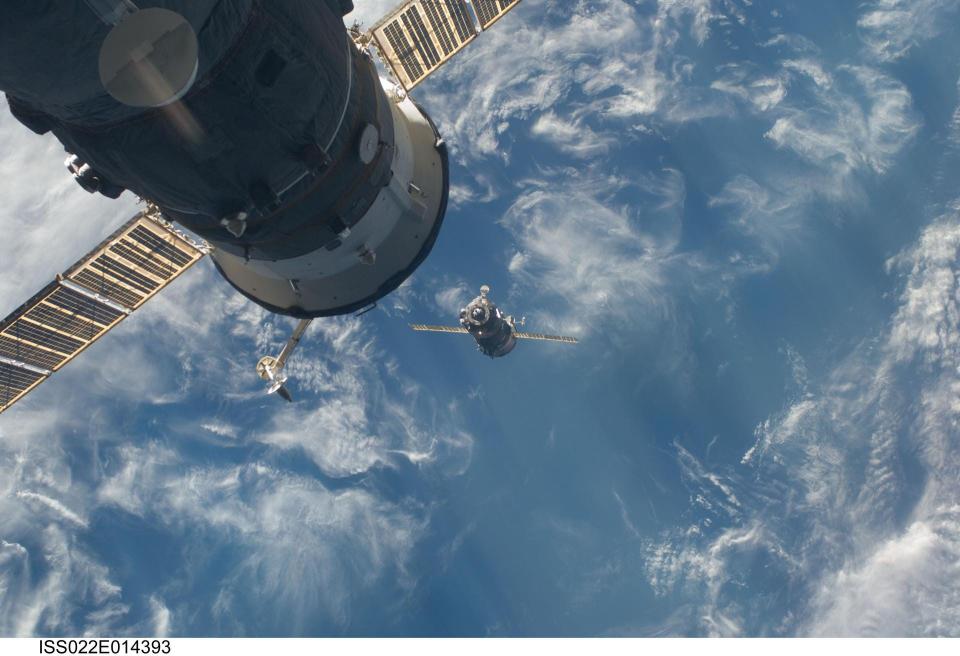 soyuz spacecraft approaches zarya module cylinder with solar panels over blue earth ocean