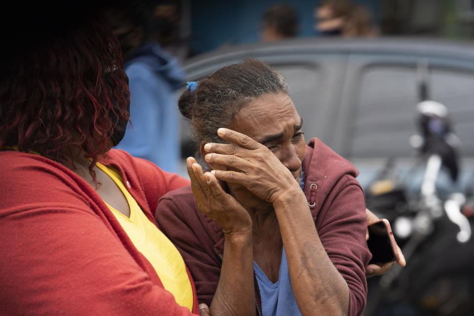 A woman is comforted as she reacts to seeing several bodies covered with linens after an armed confrontation in the Alemao slum complex in Rio de Janeiro, Brazil, Friday, May 15, 2020. According to the civil police, 10 people were found dead during the police operation against alleged drug traffickers. (AP Photo/Leo Correa)