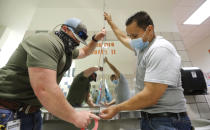 Wearing masks amid the concern of COVID-19, Richardson Independent School District workers Rogelio Ponciano, right, and Matt Attaway install a plexiglass barrier on the sink in the restroom for students at Bukhair Elementary School in Dallas, Wednesday, July 15, 2020. (AP Photo/LM Otero)