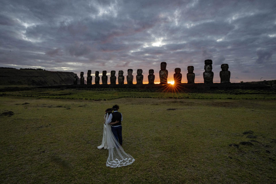 Chilean newlyweds Daniela Figueroa and Ricardo Torres, from Puerto Montt, Chile, look at moais statues at sunrise as they get cell phone photos taken by their tour guide on Ahu Tongariki, Rapa Nui, or Easter Island, Chile, Tuesday, Nov. 22, 2022. The couple spent their honeymoon on the island after COVID-19 restrictions did not allow them to hold the actual ceremony here earlier in the year. (AP Photo/Esteban Felix)