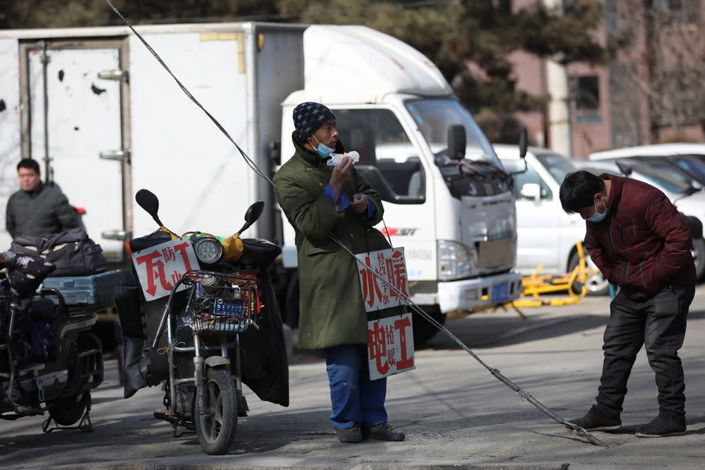 File photo: A migrant worker stands with signs advertising his work skills on a street as he waits to get hired in Shenyang, China, 25 February 2021 (AFP via Getty Images)