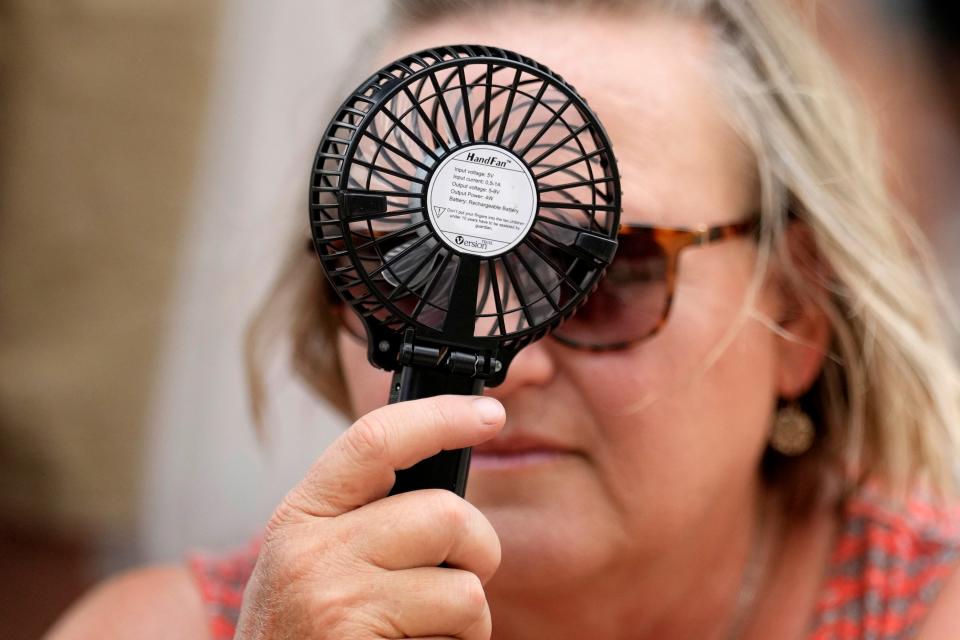 A Houston Astros fan uses a hand fan to keep cool while waiting to enter Minute Maid Park for baseball game against the Cincinnati Reds Saturday, June 17, 2023, in Houston.