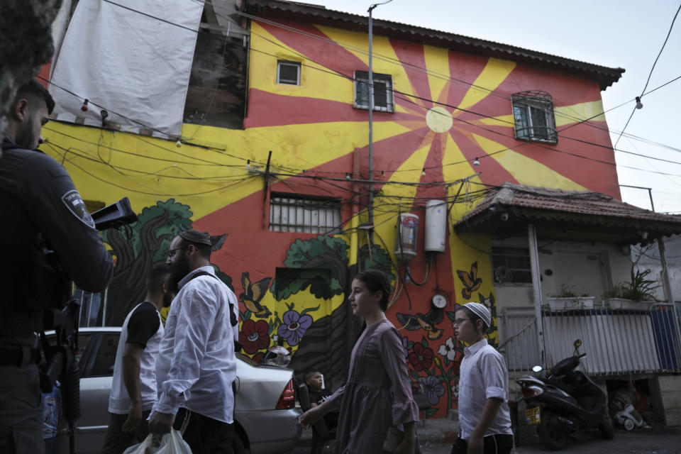 An Israeli border police officer watches Israeli Jewish settlers walk on a street lined with Palestinian homes painted in murals in the Silwan neighbourhood of east Jerusalem, Friday, Aug. 26, 2022. A group of artists has filled a Palestinian area of east Jerusalem with paintings of large, wide-open eyes. The murals are a reminder that all eyes are on the neighborhood of Silwan, a flashpoint where Palestinians say Israeli forces and settlers are working to drive them out of their homes. (AP Photo/ Mahmoud Illean)