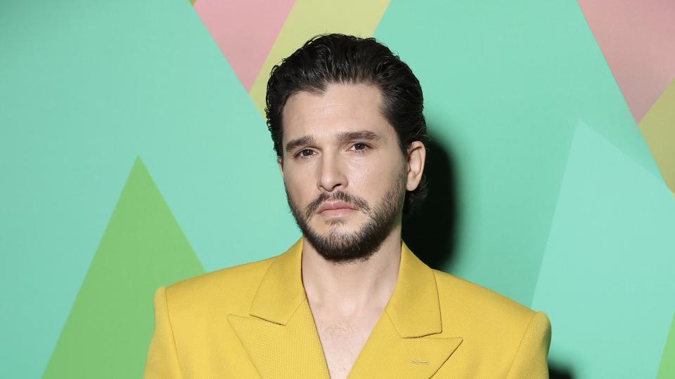 Kit Harington in a yellow jacket in front of a green background.