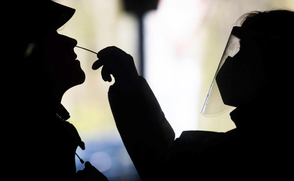 Helpers test a woman at a test center for the novel corona virus using a rapid test in Hannover, Germany, Friday, April 16, 2021. The Robert Koch Institute (RKI) continues to report an increase in new corona infections in Germany. (Julian Stratenschulte/dpa via AP)