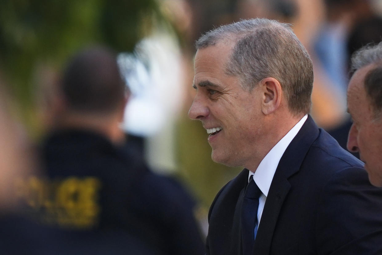 Hunter Biden, wearing a dark suit and tie, smiles as he arrives for his arraignment at federal court. 