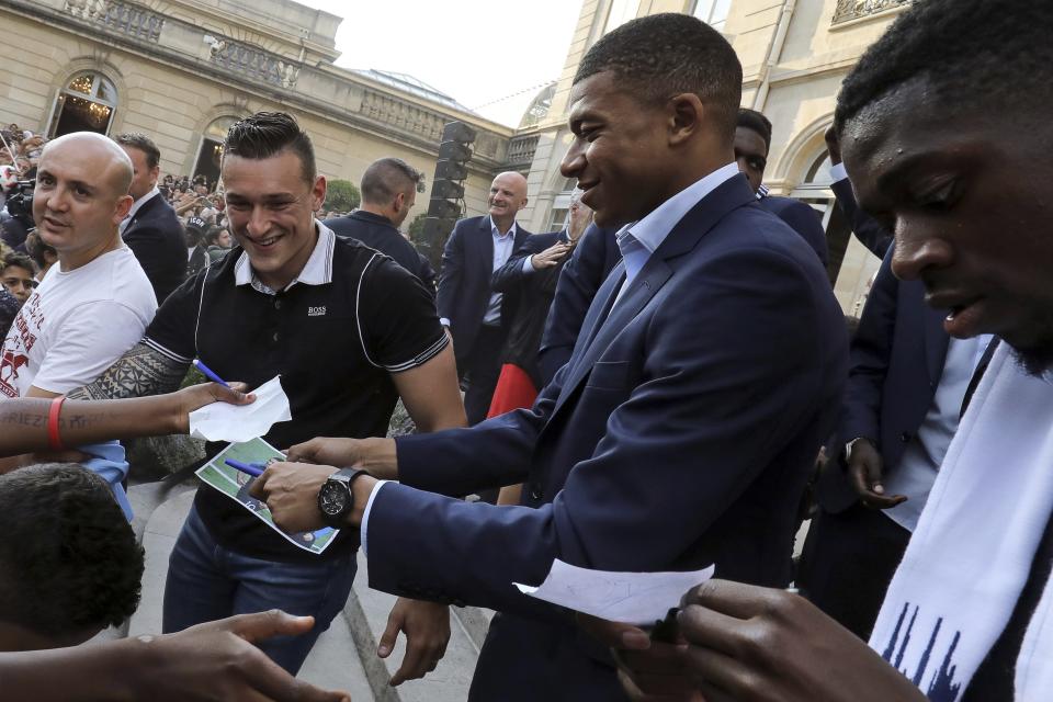 France forward Kylian Mbappe, center, and forward Ousmane Dembele sign autographs during an official reception at the Elysee Presidential Palace in Paris, Monday, July 16, 2018. France is readying to welcome home the national soccer team for a parade down the Champs-Elysees, where tens of thousands thronged after the team's 4-2 victory over Croatia Sunday. (Ludovic Marin/Pool Photo via AP)