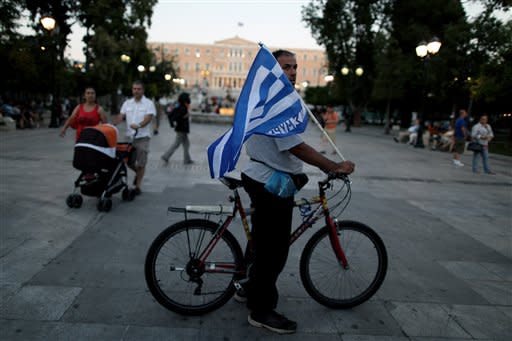 A New Democracy conservative party supporter holds a greek flag next a New Democracy party election kiosk at Syntagma square in Athens, Sunday, June 17, 2012. The pro-bailout New Democracy party came in first Sunday in Greece's national election, and its leader has proposed forming a pro-euro coalition government.(AP Photo/Petros Giannakouris)