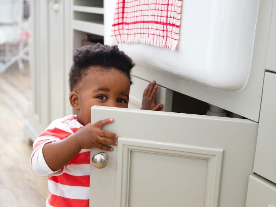 A child reaches into a kitchen cabinet filled with cleaning supplies.