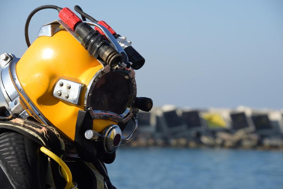 a saturation diver with a yellow helmet with water and coastline in the distance behind them