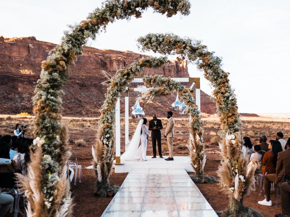 A bride and groom say their vows in front of an alter framed in flowers.
